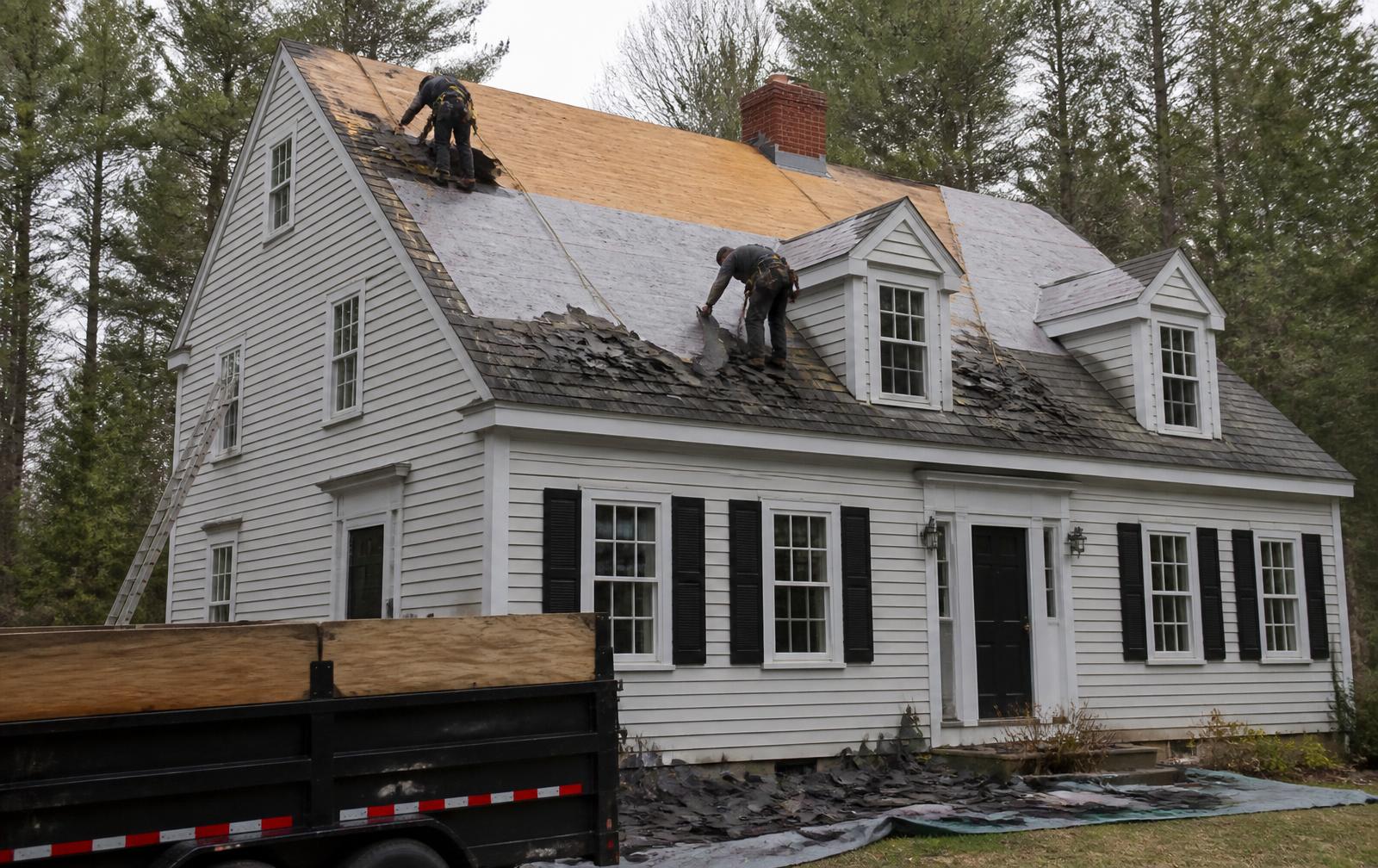Roof replacement in progress on a New England home with old shingles torn off